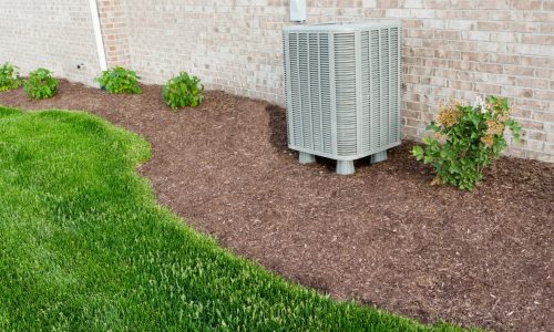 Air conditioner condenser unit standing outdoors in a garden in a neat clean mulched flowerbed for easy access for maintenance